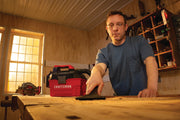 Photo of a person using a CRAFTSMAN CMCV002B wet/dry vacuum on a workbench in a woodshop, vacuum cleaning sawdust.