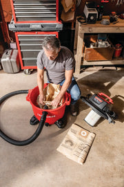 Photo of person installing a dust collection bag in a Craftsman wet/dry vacuum CMXEVBE17595, with accessories on floor.