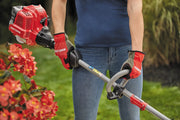 Photo of person holding Craftsman gas string trimmer CMXGTAMDSS25, red gloves, trimming near flowers outdoors.